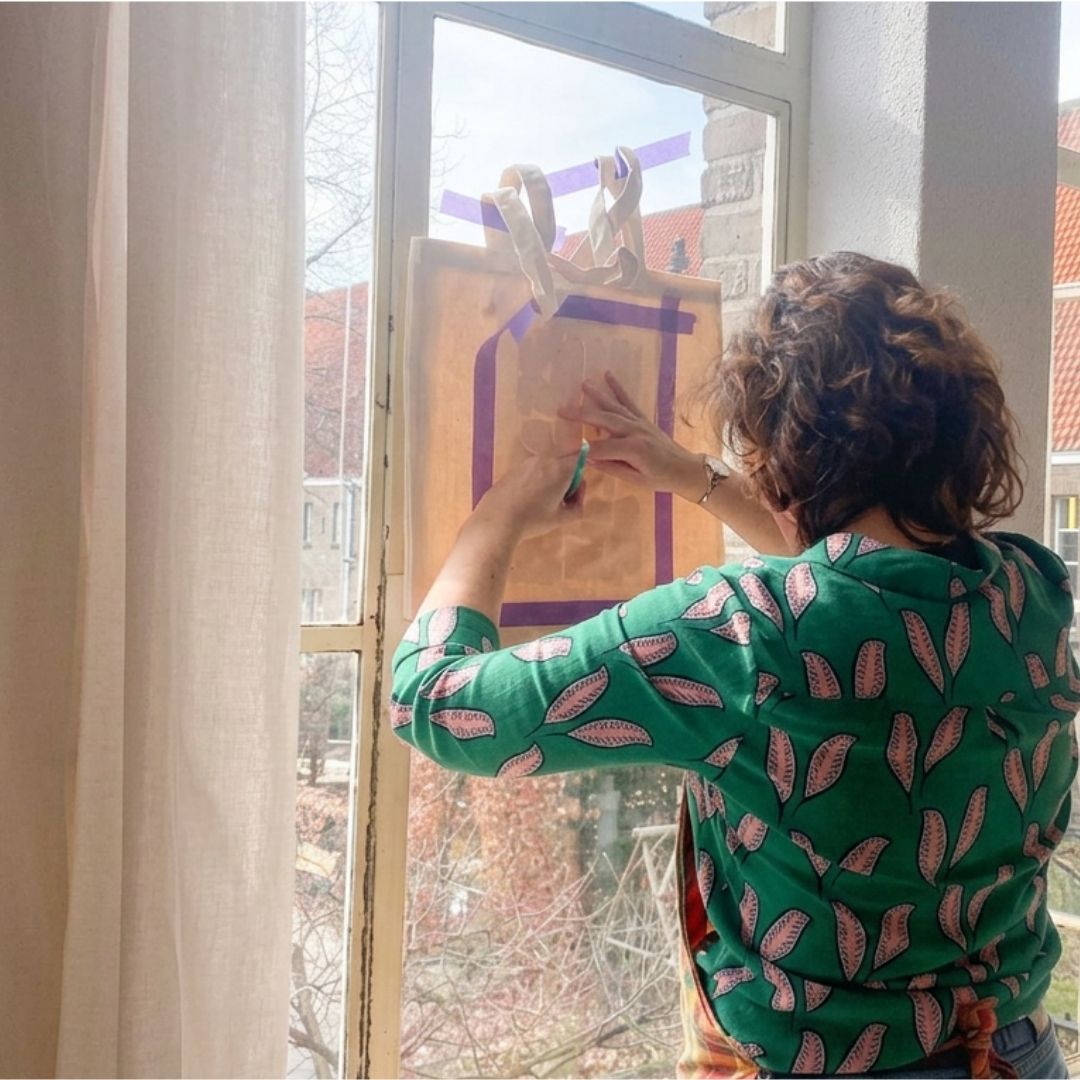 Deelnemer trekt een ontwerp over op een katoenen tas als voorbereiding op het schilderen tijdens een creatieve textiel workshop